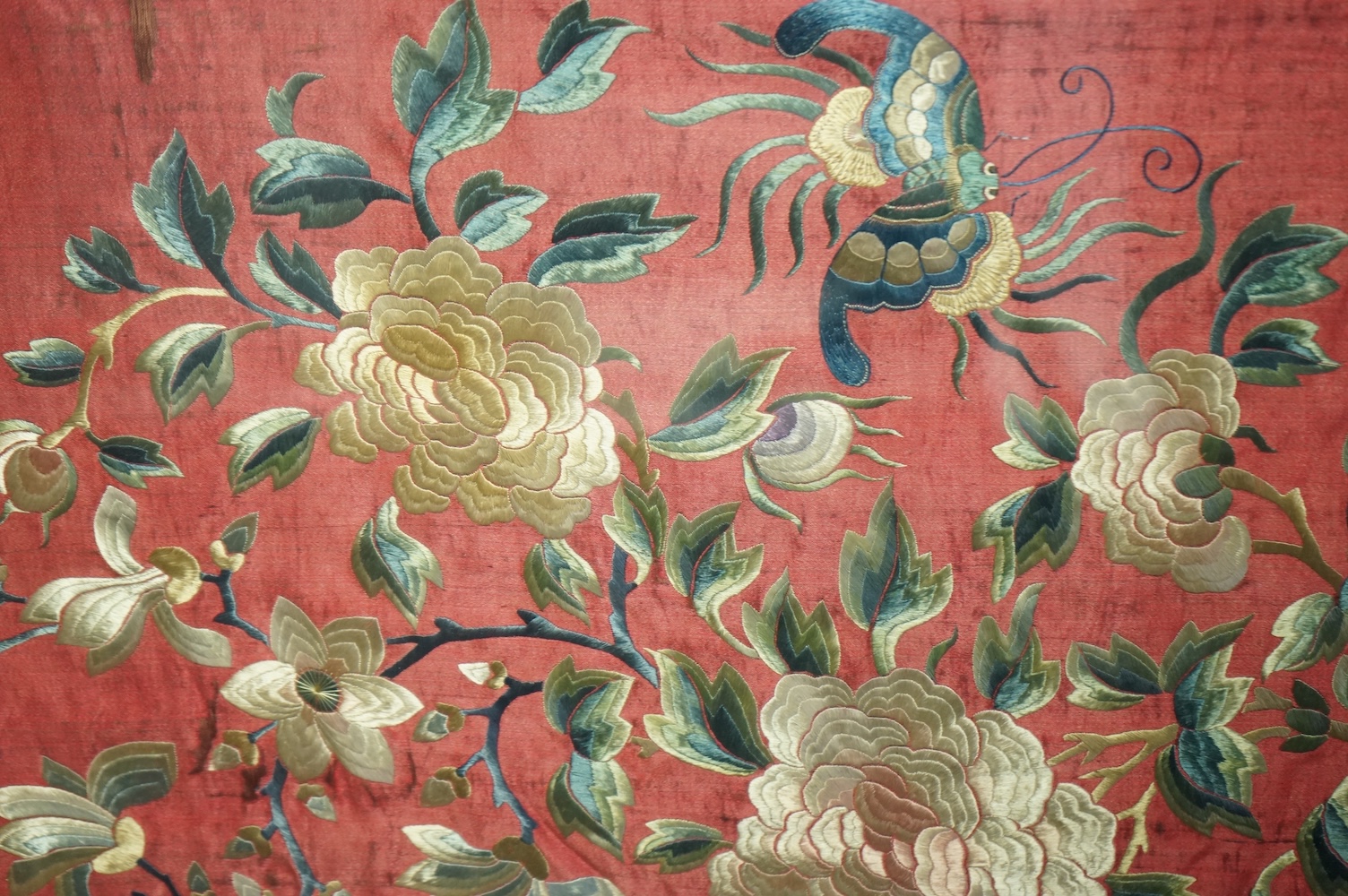 A pair of framed early 20th century Chinese silk embroideries, probably panels cut from a larger embroidery or bed cover. Embroidered with a large central cartouche of flowers birds and butterflies. 89cm x 73cm. Conditio